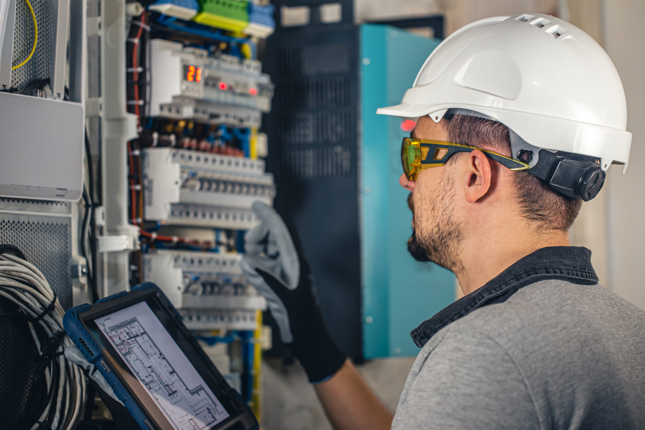 Man, an electrical technician working in a switchboard with fuses. Installation and connection of electrical equipment. Professional uses a tablet.